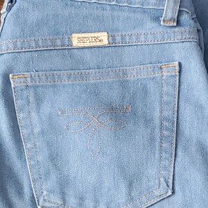 Op de afbeelding: Lichtblauwe spijkerbroek met een achterzak met een decoratief gestikt ontwerp. De jeans heeft een Sheplers-merklabel. De stiksels zijn in een contrasterende kleur en de algehele stijl is klassiek.