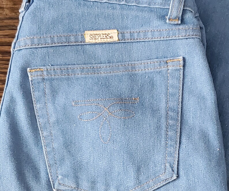 Op de afbeelding: Lichtblauwe spijkerbroek met een achterzak met een decoratief gestikt ontwerp. De jeans heeft een Sheplers-merklabel. De stiksels zijn in een contrasterende kleur en de algehele stijl is klassiek.
