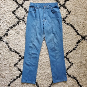 Op de afbeelding: Lichtblauwe spijkerbroek met hoge taille en rechte pijpen. De jeans heeft een klassiek ontwerp met vijf zakken en een knoop- en ritssluiting. Verticale naden lopen over de voorkant van elke broekspijp. De jeans worden gepresenteerd op een patroonkleed.