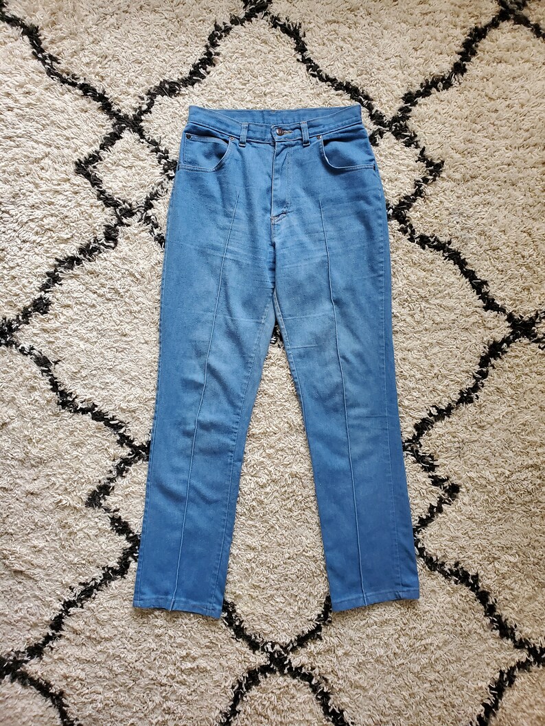 Op de afbeelding: Lichtblauwe spijkerbroek met hoge taille en rechte pijpen. De jeans heeft een klassiek ontwerp met vijf zakken en een knoop- en ritssluiting. Verticale naden lopen over de voorkant van elke broekspijp. De jeans worden gepresenteerd op een patroonkleed.