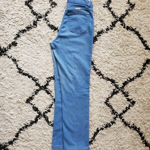 Op de afbeelding: Lichtblauwe denim jeans met een rechte pijp. De jeans heeft een klassieke vijf-zakken stijl, een ritssluiting en een klein logo op de achterzak. De jeans is netjes op een patroonkleed gevouwen.