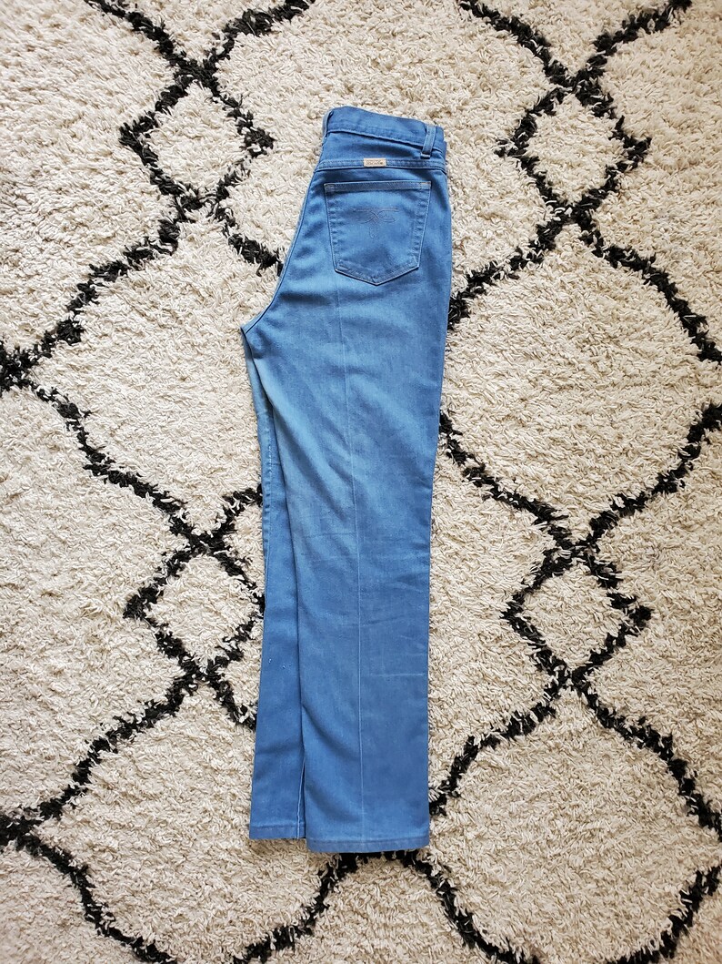 Op de afbeelding: Lichtblauwe denim jeans met een rechte pijp. De jeans heeft een klassieke vijf-zakken stijl, een ritssluiting en een klein logo op de achterzak. De jeans is netjes op een patroonkleed gevouwen.