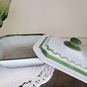May include: White ceramic serving dish with a green rim and lid. The lid has a green knob and a scalloped edge.