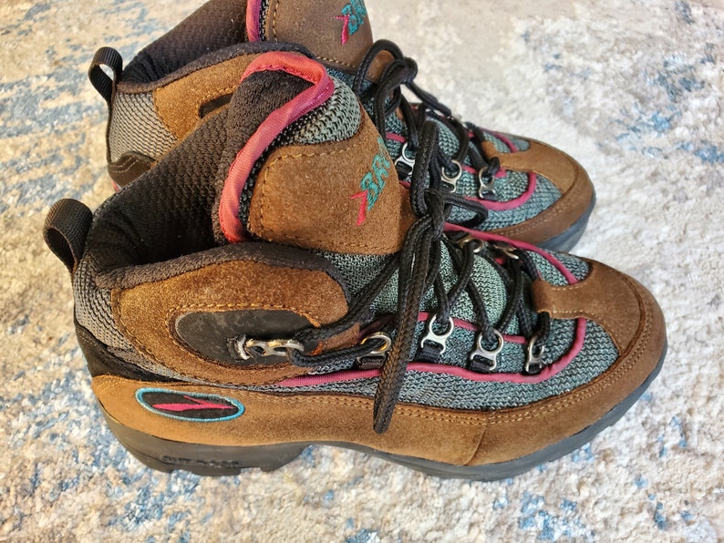 Peut inclure: Bottes de randonn&eacute;e marron avec des accents turquoise et rose. Les bottes ont une fermeture &agrave; lacets et une semelle ext&eacute;rieure robuste.