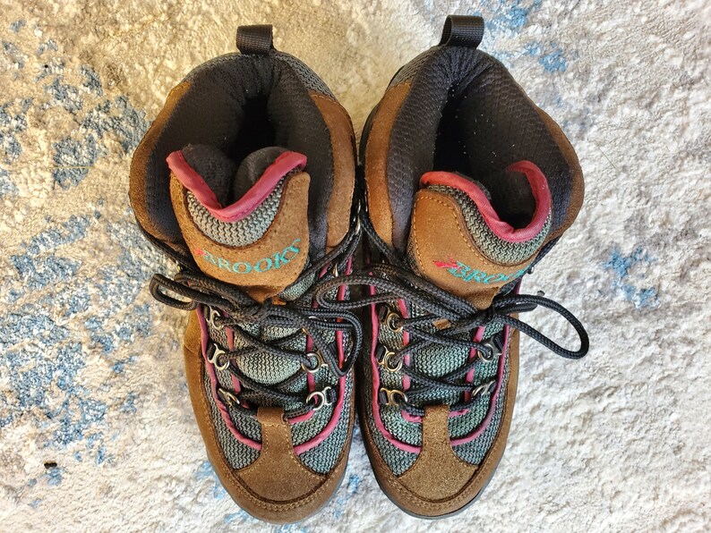 Peut inclure: Une paire de chaussures de randonn&eacute;e brunes avec des accents turquoise et roses. Les chaussures ont des lacets noirs et le mot "Brooks" est &eacute;crit sur le c&ocirc;t&eacute;.