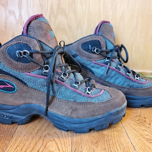Peut inclure: Une paire de bottes de randonn&eacute;e marron avec des accents bleus et rouges. Les bottes ont une tige en mesh et en daim et une semelle ext&eacute;rieure en caoutchouc noir. Les bottes ont une fermeture &agrave; lacets et le texte "OUTDOOR" est imprim&eacute; sur le c&ocirc;t&eacute;.