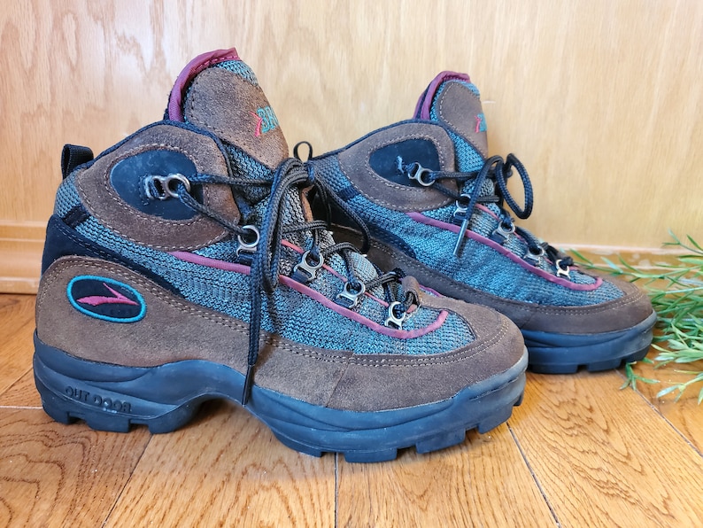 Peut inclure: Une paire de bottes de randonn&eacute;e marron avec des accents bleus et rouges. Les bottes ont une tige en mesh et en daim et une semelle ext&eacute;rieure en caoutchouc noir. Les bottes ont une fermeture &agrave; lacets et le texte "OUTDOOR" est imprim&eacute; sur le c&ocirc;t&eacute;.