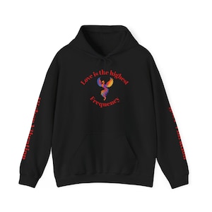 Op de afbeelding: Zwarte hoodie met een kleurrijke phoenix-afbeelding en de tekst "Love is the highest Frequency". De mouwen hebben de tekst "Higher Vibration" en "Higher Vibration" in het rood. Voorzien van een capuchon met trekkoord en een voorzak.