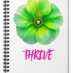 Puede incluir: Cuaderno de espiral blanco con una ilustración de una flor verde vibrante y la palabra "THRIVE" en rosa. La flor tiene un centro amarillo y gotas de agua.