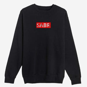 May include: Black crewneck sweatshirt with the word "SABR" in a red rectangular box. The text is in white, stylized lettering. The sweatshirt has long sleeves and a classic, casual design.