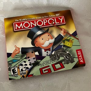 May include: A Monopoly PC CD-ROM game box featuring the Monopoly mascot in a top hat and tuxedo. The cover displays the Monopoly logo, the Atari brand, and the ESRB Everyone rating. Graphics include dice, a metal car token, and a ten-dollar bill.