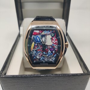 Könnte beinhalten: Eine roségoldene Franck Muller Yachting Uhr mit einem schwarzen Lederarmband. Das Zifferblatt der Uhr zeigt ein farbenfrohes Graffiti-Design. Die Uhr wird in einer schwarzen Box mit strukturierter Außenseite präsentiert.