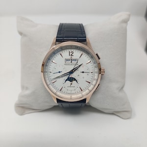 May include: A luxury wristwatch with a white face, gold-coloured case, and a dark blue leather band. The watch features multiple subdials, a date display, and the text "12" and "2027 FEB". The watch is displayed on a white pillow.