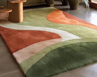 May include: A modern living room featuring a large, abstract-patterned rug in shades of green, orange, and cream. The rug is the focal point, complemented by a green sofa, wooden side tables, and potted plants, creating a warm, inviting atmosphere.
