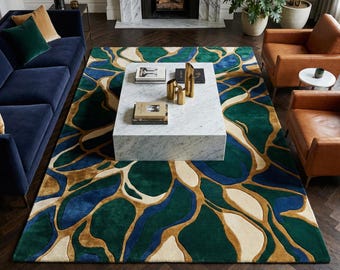May include: A large area rug with an abstract design in shades of green, blue, gold, and cream. The rug is placed in a living room setting with a blue sofa, leather armchairs, and a marble coffee table.