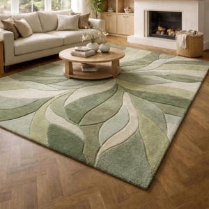 Könnte beinhalten: Ein großer Teppich mit einem Blattmuster in Grün- und Beigetönen. Der Teppich liegt auf einem Holzboden in einem Wohnzimmer, mit einem Sofa, einem Couchtisch und einem Kamin im Hintergrund.