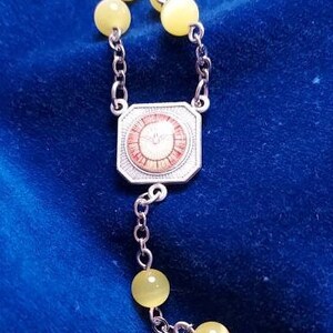 May include: A silver rosary with yellow beads and a silver centrepiece featuring a red and white design.