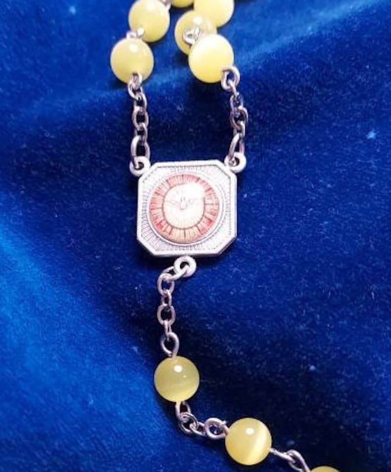 May include: A silver rosary with yellow beads and a silver centrepiece featuring a red and white design.
