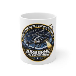 May include: White ceramic mug featuring a detailed illustration of a police helicopter with the text "DON'T MAKE ME GET OUT OF THE CHOPPER" and "AIRBORNE LAW ENFORCEMENT". The design includes a night sky and forest.