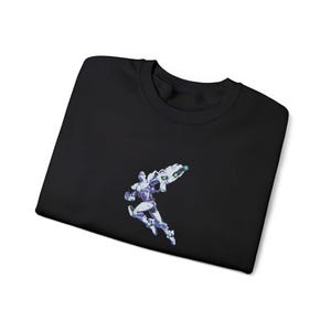 Peut inclure: Sweat-shirt noir à col rond avec un motif brodé d'un personnage futuriste blanc, violet et vert. Le personnage tient une grande arme. Le sweat-shirt est fait d'une matière douce.