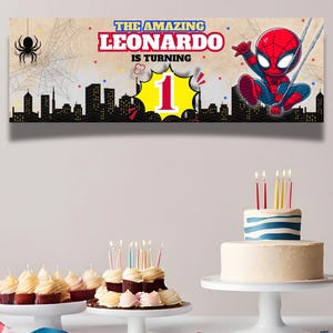 May include: A birthday banner featuring Spider-Man with the text "THE AMAZING LEONARDO IS TURNING 1". The banner has a cityscape silhouette and a spider web design. Cupcakes and a cake with candles are also visible.
