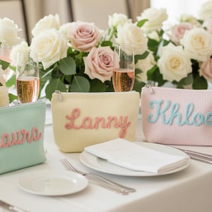 Puede incluir: Tres estuches rectangulares con cremallera hechos de tela acanalada en verde menta, amarillo p&aacute;lido y rosa claro. Cada estuche presenta un nombre bordado en un color contrastante: Laura en rosa, Lanny en rosa y Khloe en azul claro.