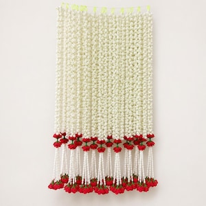 May include: A decorative wall hanging featuring multiple vertical strands of small white flowers. Each strand is accented with a bright red flower at the top and bottom, suspended from a thin horizontal wire with small lime green loops.