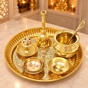 May include: A polished brass set featuring a large round tray with an intricate floral pattern, a tall bell, a small incense burner, a deep bowl with a long-handled spoon, and two small open dishes, all arranged together on a flat surface.