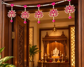 May include: A decorative door hanging garland featuring a horizontal string of white beads interspersed with bright pink pom-poms. Five hanging lotus flower ornaments in pink and gold with central mirror accents are suspended from the main strand.