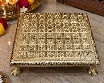 May include: A square gold-colored metal pedestal stand featuring a repeating embossed floral grid pattern on the top surface, a twisted rope-style border, and four small rounded feet. The word CRAFTINGO is printed in the bottom right corner.