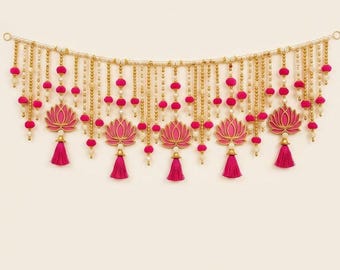 May include: A decorative wall hanging featuring a horizontal string of cream-colored beads interspersed with vibrant pink pom-poms. Five pink lotus-shaped cutouts are suspended from the main strand, each finished with a matching pink tassel.