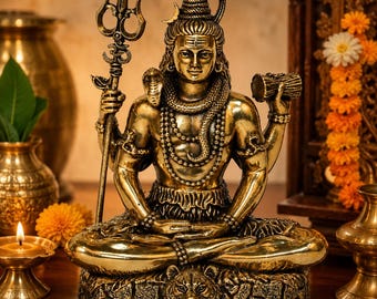 May include: A metallic gold-toned statue of the deity Shiva seated in a meditative pose. The figure holds a trident in the right hand and a small drum in the left, with a cobra coiled around the neck and a tiger skin base beneath the figure.