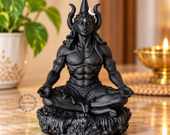May include: A matte black statue of a deity in a meditative lotus position, featuring a crescent moon on the head, a snake coiled around the neck, and beaded necklaces. The figure has defined musculature and sits on a textured base.