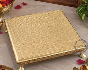 May include: A square gold-colored metal display stand featuring an embossed grid pattern across the top surface and decorative edges. The stand is supported by four small, ornate feet and includes a circular logo with the text CRAFTINGO.