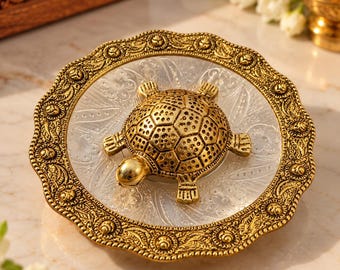 May include: A circular decorative tray featuring a clear glass center with etched floral patterns and a wide, scalloped gold-tone metal rim. A three-dimensional gold-tone metal turtle figure is centered on the glass surface.
