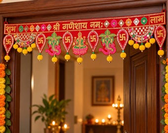 May include: A red fabric door hanging featuring gold embroidered text, swastika symbols, and depictions of Ganesha and Lakshmi. The decorative valance is adorned with small mirrors, colorful floral patterns, and yellow pom-pom fringe trim.