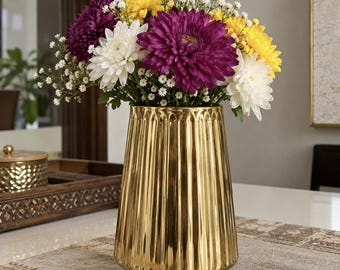 May include: A gold-colored, metallic, fluted vase with a tapered cylindrical shape. The vase is filled with a bouquet of purple, white, and yellow chrysanthemums mixed with small white baby's breath flowers. The word CRAFTINGO is printed at the base.