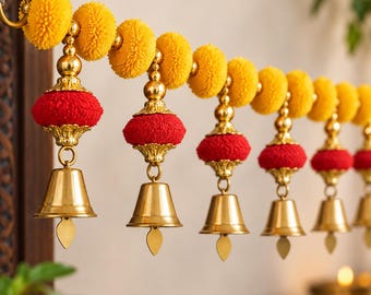 May include: A decorative garland featuring a horizontal string of bright yellow pom-poms interspersed with gold-toned metal beads. Hanging from the string are several red fabric pom-poms, each topped with a gold-toned cap and a brass bell.