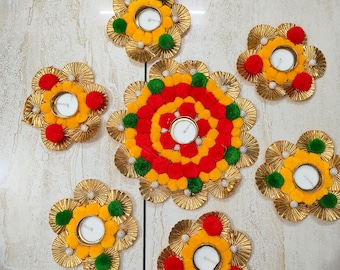 May include: A set of six decorative candle holders featuring gold pleated paper petals arranged in a flower shape. Each holder contains a white tea light candle and is accented with small red, yellow, and green pom-poms around the center.