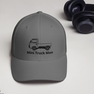 Puede incluir: Una gorra de béisbol gris con una imagen bordada en negro de un camión pequeño y el texto "Mini Truck Man".