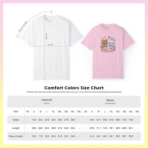 Puede incluir: Se muestran dos camisetas, una blanca y otra rosa, con una tabla de tallas que detalla las medidas en pulgadas y cent&iacute;metros. La camiseta rosa presenta un dise&ntilde;o de gato de dibujos animados horneando. La tabla incluye medidas de ancho, largo y largo de manga para varias tallas.