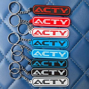 May include: A collection of keychains with the word "ACTY" in bold, white lettering. The keychains come in various colors, including red, white, blue, black, and white. Each keychain has a metal ring and chain.