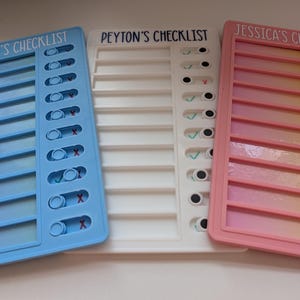 May include: Three rectangular plastic checklist boards in light blue, white, and pink. Each board features a personalised name at the top: HARRY'S CHECKLIST, PEYTON'S CHECKLIST, and JESSICA'S CHECKLIST. Each includes ten sliding toggles.