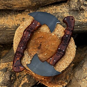 K&ouml;nnte beinhalten: Zwei gebogene Handbeile mit mattschwarzen Stahlklingen und dunkelbraunen Holzgriffen. Die Griffe weisen komplizierte, lasergravierte geometrische Muster auf und sind mit kleinen silbernen Nieten befestigt. Die Beile sind kreisf&ouml;rmig angeordnet.