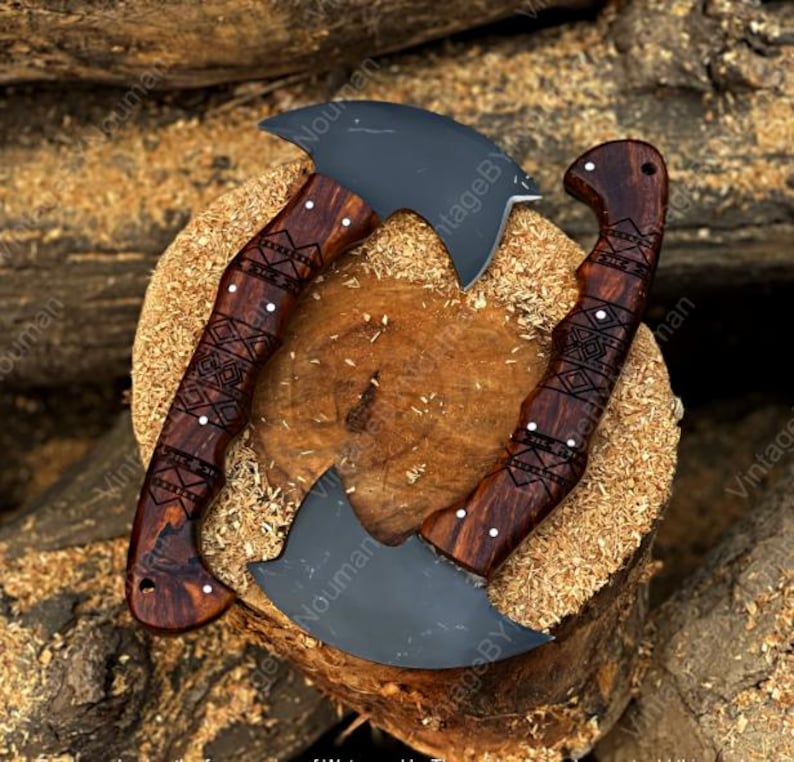 K&ouml;nnte beinhalten: Zwei gebogene Handbeile mit mattschwarzen Stahlklingen und dunkelbraunen Holzgriffen. Die Griffe weisen komplizierte, lasergravierte geometrische Muster auf und sind mit kleinen silbernen Nieten befestigt. Die Beile sind kreisf&ouml;rmig angeordnet.