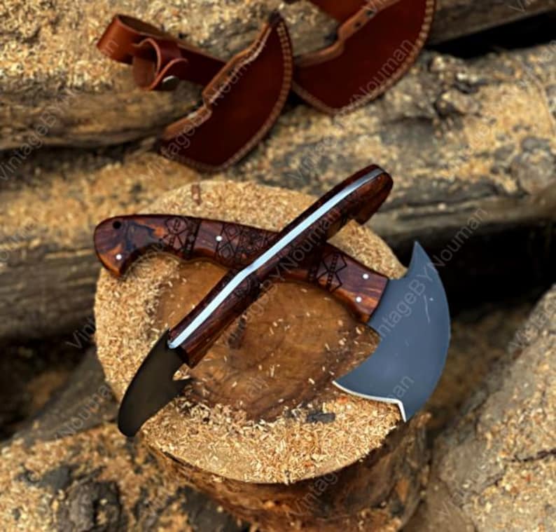 K&ouml;nnte beinhalten: Zwei halbmondf&ouml;rmige Messer mit dunklen Metallklingen und polierten Holzgriffen, die mit komplizierten geometrischen Gravuren versehen sind. Die Messer sind kreuzf&ouml;rmig angeordnet und werden von zwei braunen Lederscheiden mit Druckkn&ouml;pfen begleitet.