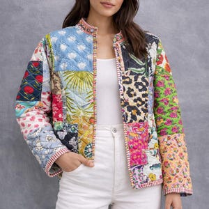 May include: A colourful patchwork jacket featuring floral, leaf, and animal prints. The jacket has a round collar and is trimmed with red and white striped fabric. The model is wearing white trousers.