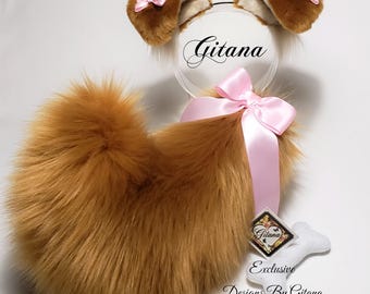 May include: A set of brown faux fur animal ears on a clear headband and a matching brown faux fur tail with a large pink satin bow. The ears feature small pink bows. A white bone-shaped tag displays the text Gitana Exclusive Designs By Gitana.