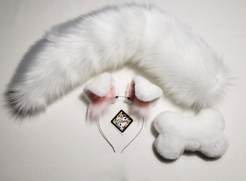 May include: White faux fur tail, pink and white faux fur cat ears headband, and a white faux fur bone. The headband has a black elastic band and a small tag that says "Gilana".