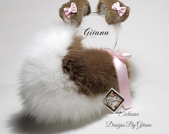 May include: A set of brown and white faux fur animal ears on a headband, accented with small pink satin bows. A large, fluffy white and brown faux fur tail is attached with a pink satin ribbon. The text Gitana and Exclusive Designs By Gitana is visible.